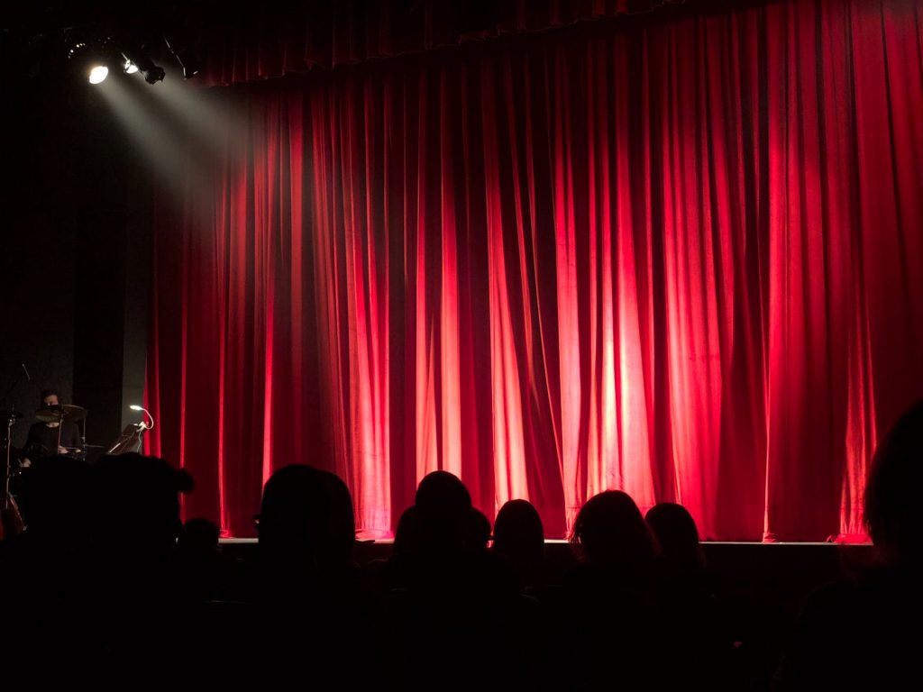 Picture of a stage with an audience waiting and a spotlight shining on an empty stage.